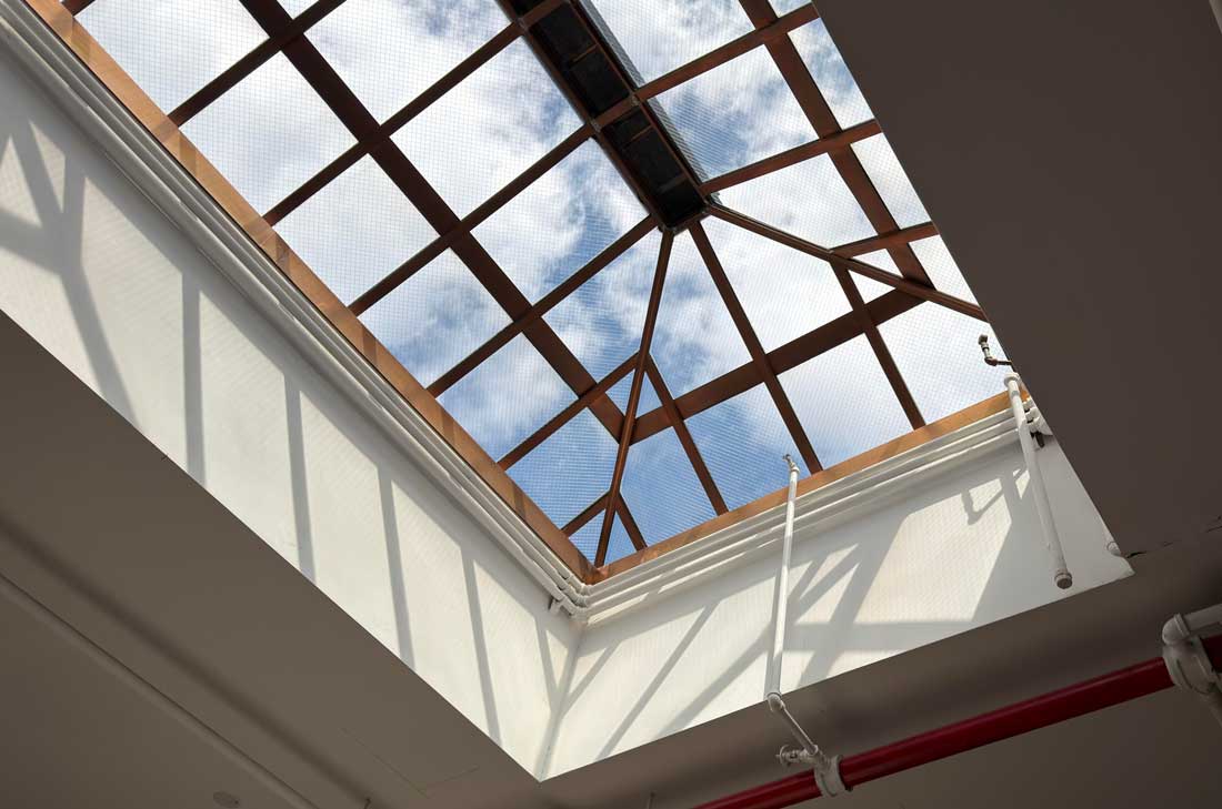 Upward view of a modern glass skylight with a geometric steel framework and natural daylight filtering into the interior space.