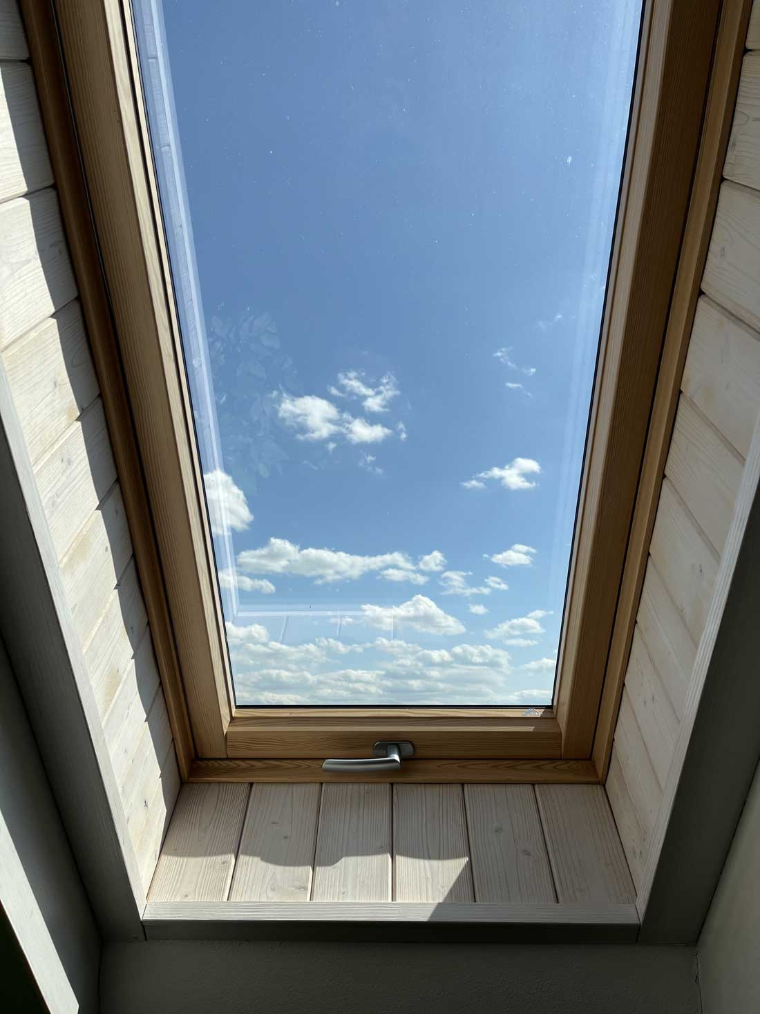 View through a skylight window with a wooden frame in an attic interior.
