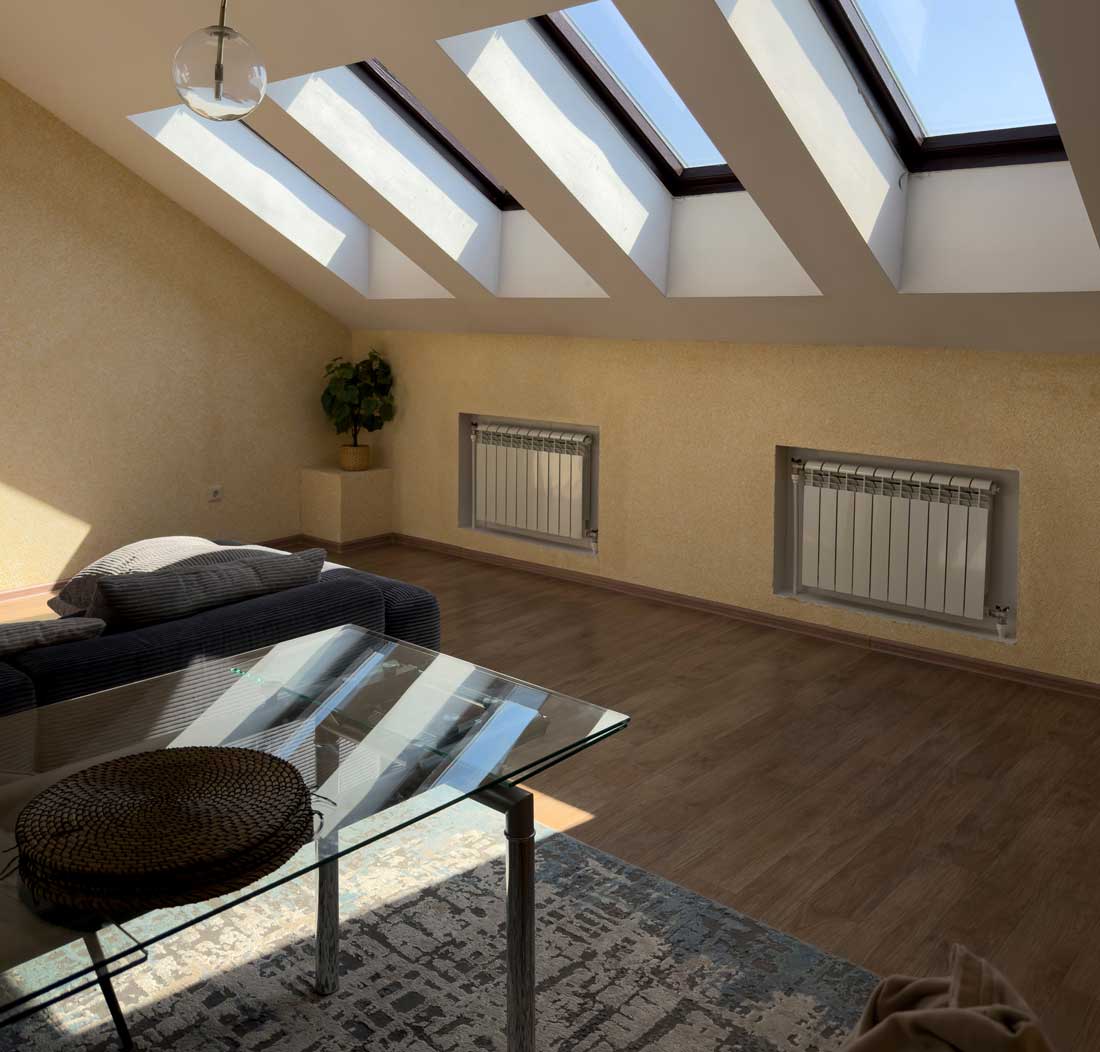Bright and spacious attic living room featuring skylights and minimalistic furniture for relaxation.